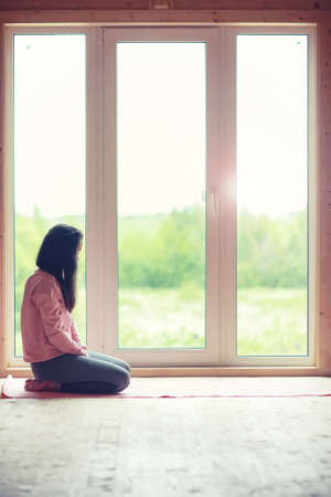 The girl is engaged in yoga on the rug in front of the windowの写真素材