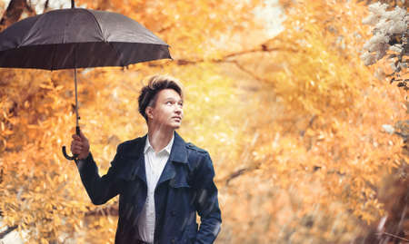 Autumn rainy weather and a young man with an umbrellaの写真素材