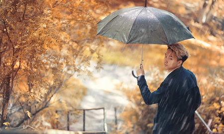 Autumn rainy weather and a young man with an umbrellaの写真素材