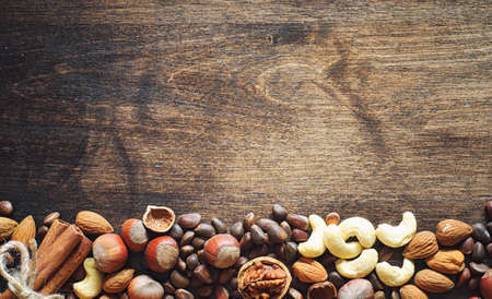 Different nuts on a wooden table. Cedar, cashew, hazelnut, walnuts and a spoon on the table. Many nuts are inshell and chistchenyh on a wooden backgroundの写真素材
