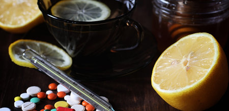 Drugs and pills on a wooden table. Various means to prevent colds. Tea with lemon and honey. Glass cup with tea slice of lemon and a jar of honey.の写真素材