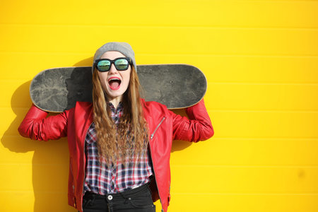 A young hipster girl is posing with a skateboard.