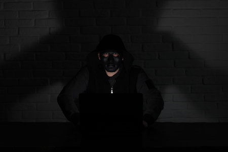 Hacker in black mask and hood at the table