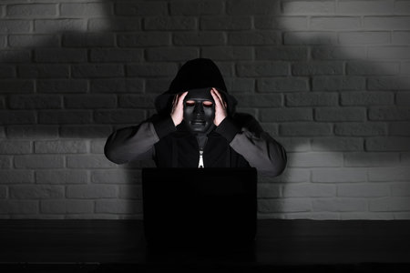 Hacker in black mask and hood at the table