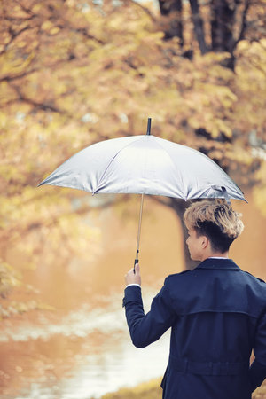 Autumn rainy weather and a young man with an umbrellaの写真素材