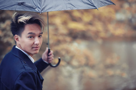 Autumn rainy weather and a young man with an umbrellaの写真素材