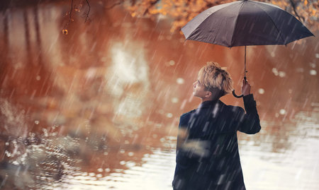 Autumn park in rainy weather and a young man with an umbrella