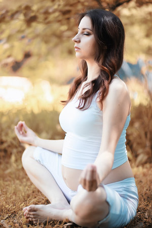 Pregnant woman doing yoga exercise in autumn