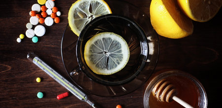 Pills on a wooden table. Tea with lemon and honey in a cup and a jar of honey.