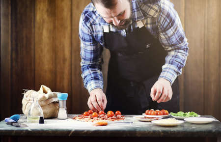 man in an apron preparing a pizza, knead the dough and puts ingrの写真素材