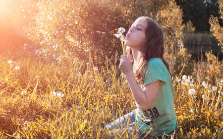 Teen blowing seeds from a dandelion flower in a parkの写真素材