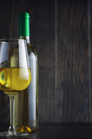 Transparent bottle of white dry wine on the table. White wine glass on a wooden background.の写真素材