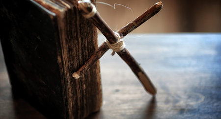 Religious old book on a wooden table. A religious cross tied with a rope and burlap next to bible....