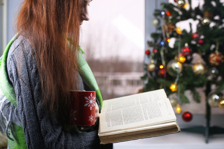 Girl with a cup of hot drink stands in front of a window in the New Year's Eveの写真素材