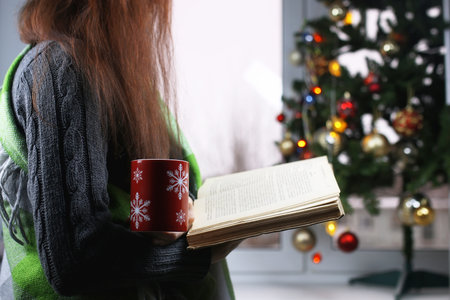 Girl with a cup of hot drink stands in front of a window in the New Year's Eveの写真素材