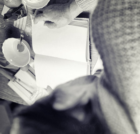 Open recipe book in the hands of an elderly woman in front of a table with utensils