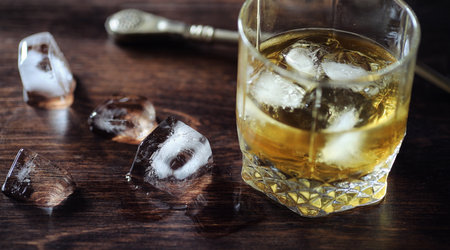Whiskey with ice with a glass. Cubes of ice on a wooden table and a glass with chilled strong alcohol. Table with American whiskey, bourbon and cards.の写真素材