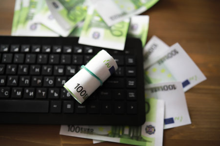 Computer keyboard and a scattering of 100 euro bills on the table. The work of a programmer and blogger on Internet.の写真素材