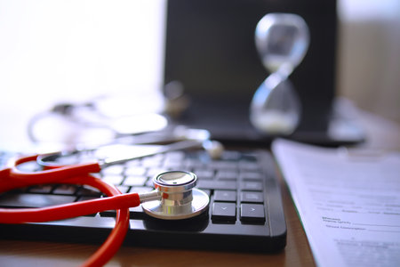 Doctor at his desk in the clinic's office. Stethoscope, test tubes, laptop, prescriptions, glasses on table.の写真素材