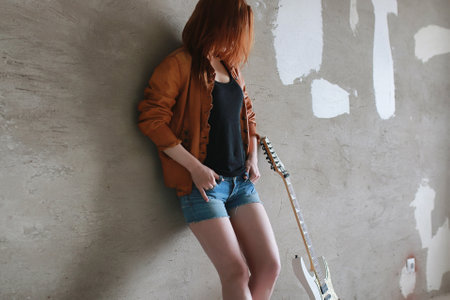 Young red-haired girl with electric guitar. Rock musician girl in a leather jacket. She is a singer and a performer of rock music.の写真素材