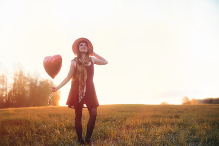 A girl in a hat on a walk in the park. A girl with a basket walks in autumn. Girl is walking along the road at sunset.の写真素材