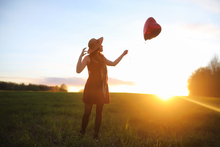 A girl in a hat on a walk in the park. A girl with a basket walks in the spring. Girl is walking along the road at sunset.の写真素材