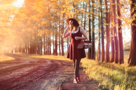 A girl in a hat on a walk in the park. A girl with a basket walks in autumn. Girl is walking along the road at sunset.の写真素材