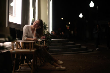 Young beautiful girl sitting in a street cafe at nightの写真素材