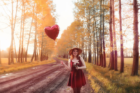 A girl in a hat on a walk in the park. A girl with a basket walks in autumn. Girl is walking along the road at sunset.の写真素材