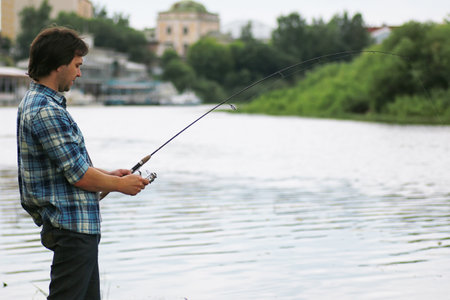 A man with a beard is fishing for spinning in the riverの写真素材