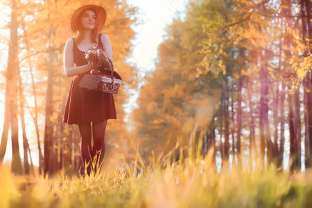 A girl in a hat on a walk in the park. A girl with a basket walks in autumn. Girl is walking along the road at sunset.の写真素材