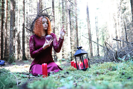 The red-haired witch holds a ritual with a crystal ball in the forestの写真素材