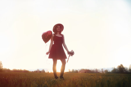 A girl in a hat on a walk in the park. A girl with a basket walks in autumn. Girl is walking along the road at sunset.の写真素材