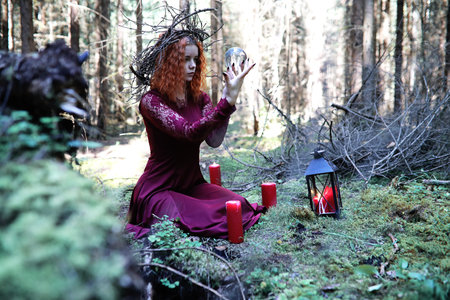 The red-haired witch holds a ritual with a crystal ball in the forestの写真素材