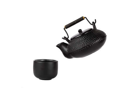 Textured clay teapot for brewing tea and a cup. The teapot hangs over the cup on a slope. Isolate.の写真素材