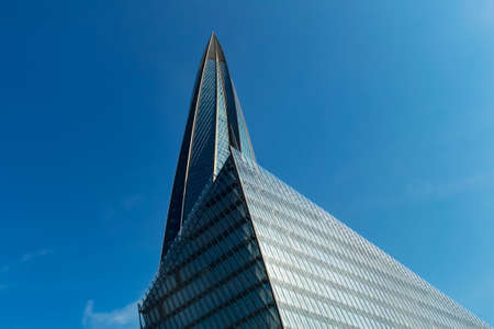 The spire of the office building is made of glass against the blue sky.の写真素材