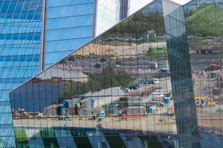 The glass facade of the building which reflects the construction site in front of it on a sunny day