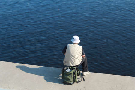 A lone fisherman on the city embankment catches fish.の写真素材