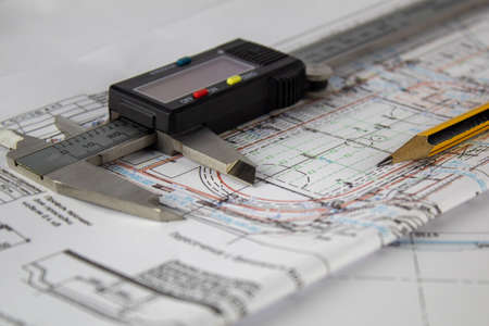 A caliper and a pencil lie on a fragment of a construction drawing.