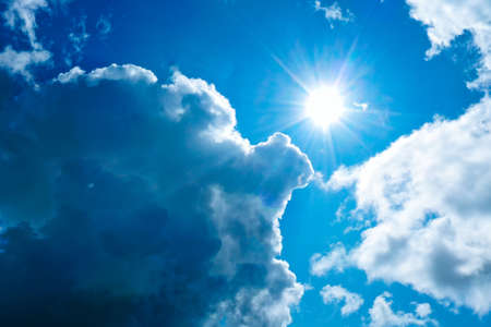 Bright sun in thick blue clouds against a blue sky.