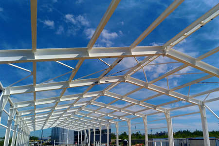 Low angle view of green metal roof of industrial building structure in construction site against blue sky backgroundの写真素材