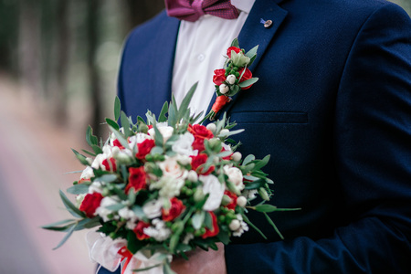 The groom in a dark blue jacket holds a bouquet of rosesの写真素材