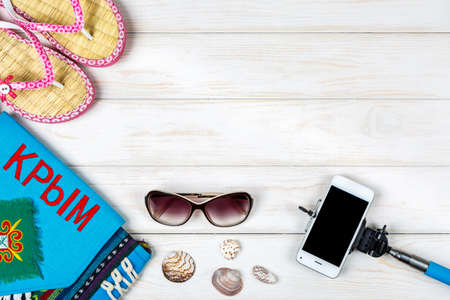 View of flip-flops, seashells, phone, sunglasses, travel bag with writing "Crimea" in russian lying on white wooden background.の写真素材