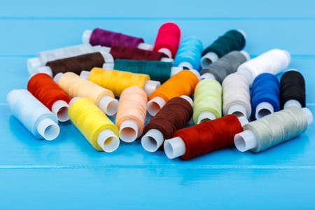 Spools of thread, randomly lying on a blue wooden background.