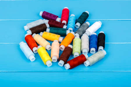 Spools of thread, randomly lying on a blue wooden background.