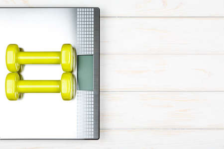 Dumbbells lying on the scales on white wood background. Concept plan.
