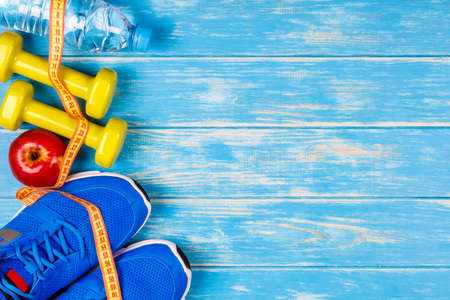 Bottle of water, dumbbells, sport shoes, measure tape and apple on blue wood background.の写真素材