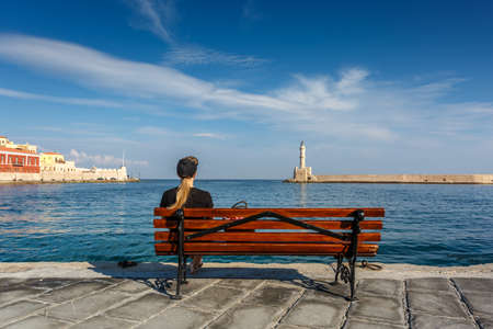 Girl sitting on bench and looking at sea. Focus on girl.の写真素材