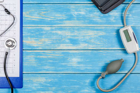 Stethoscope, blood pressure meter, an electrocardiogram on a blue wooden background.