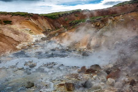 View of steaming hot springs in Iceland on the background of colorful mountainsの写真素材